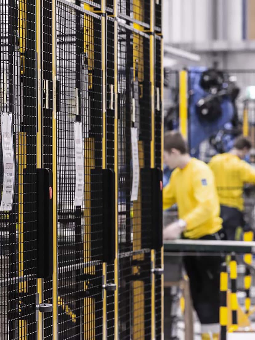 A row of machine safety enclosures with secure mesh panels in an industrial workspace. The image highlights key factors in choosing machine guards, such as visibility, accessibility, and protection, to ensure a safe and efficient work environment.