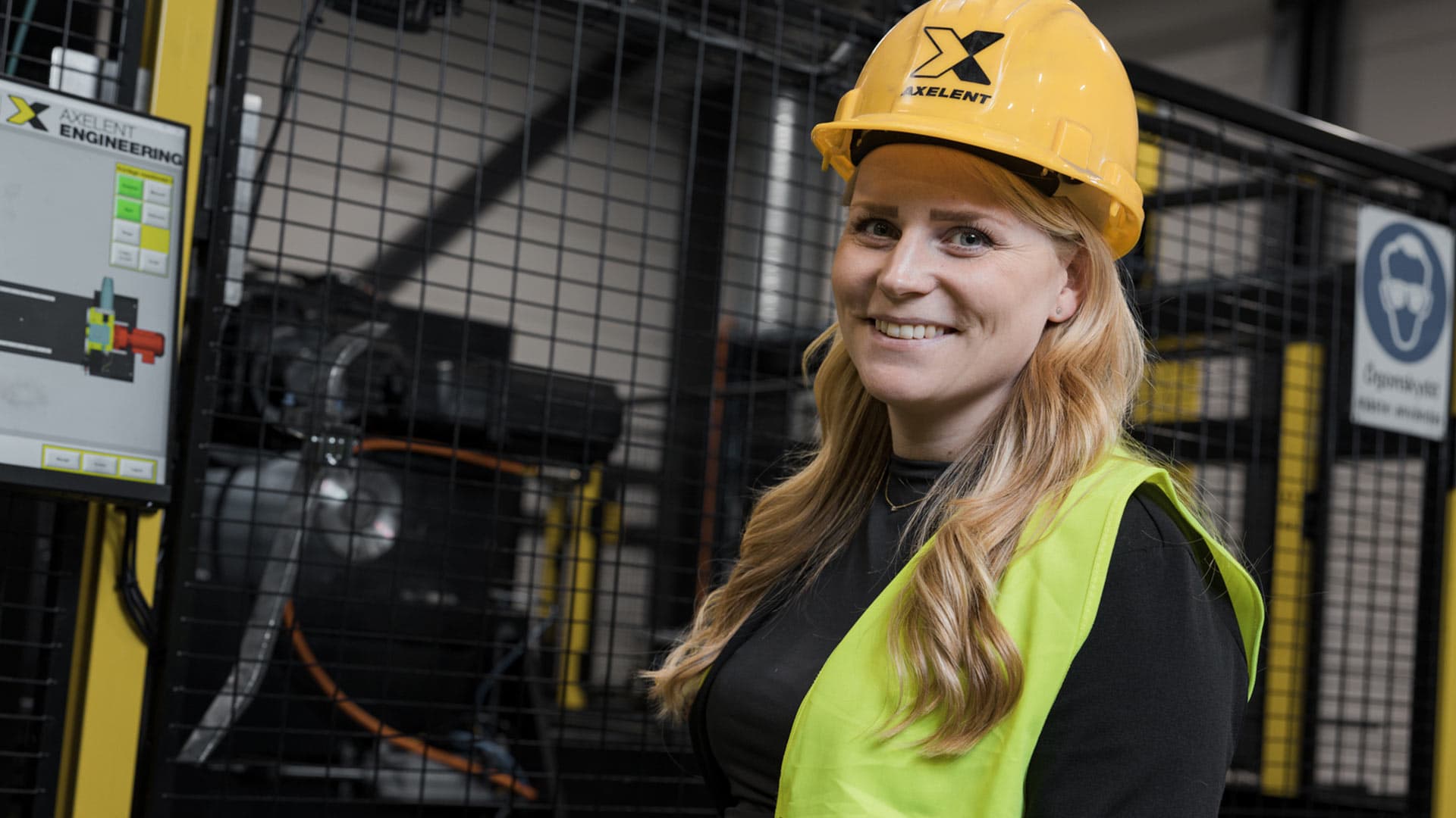 Employee wearing a hard hat and high-visibility vest standing next to machine guarding in an industrial environment