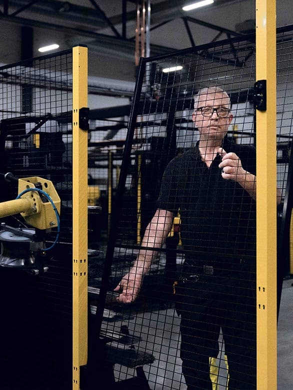 A worker removing a protective safety fence in an industrial setting, with a robotic arm visible in the background. The image highlights the importance of machine safety measures, ensuring controlled access to hazardous areas and preventing workplace accidents.