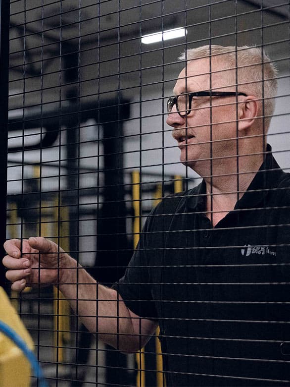 A man in an industrial setting mounting a protective safety fence in black mesh. The image highlights the importance of machine safety barriers in preventing accidents and ensuring a secure working environment.