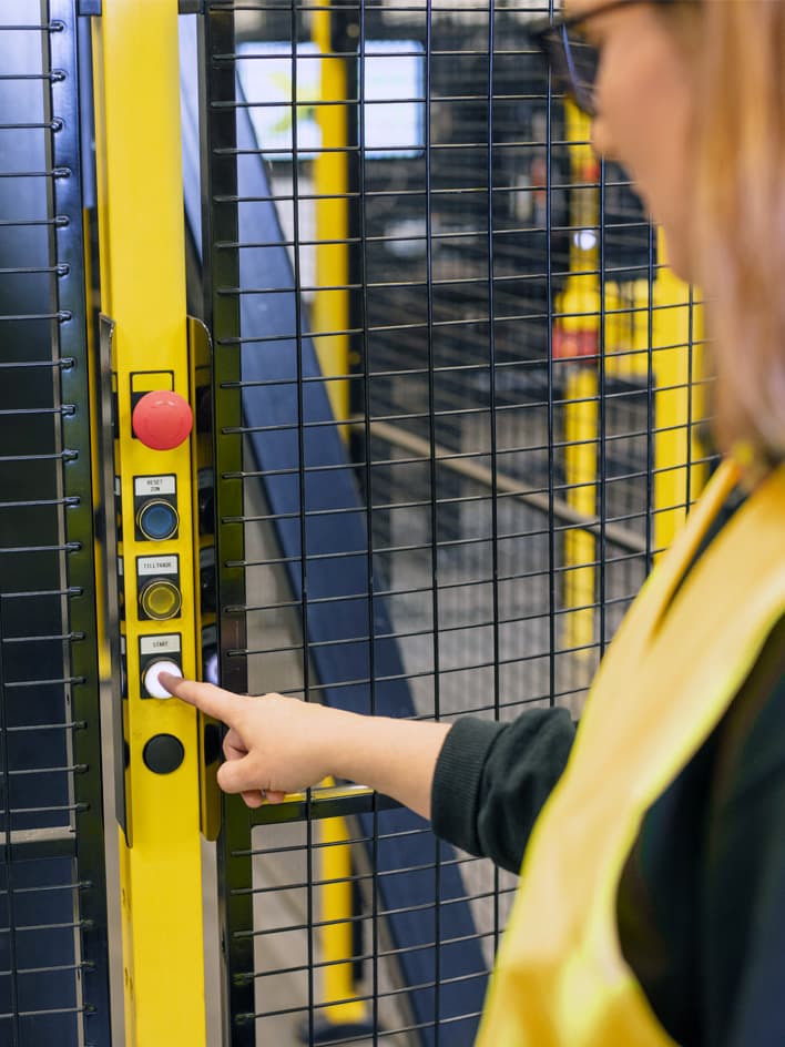 A worker in a high-visibility vest pressing the start button on a control panel mounted on a machine safety fence. The image highlights the importance of selecting machine guards with integrated safety features, such as access controls and emergency stop functions, to ensure workplace safety.