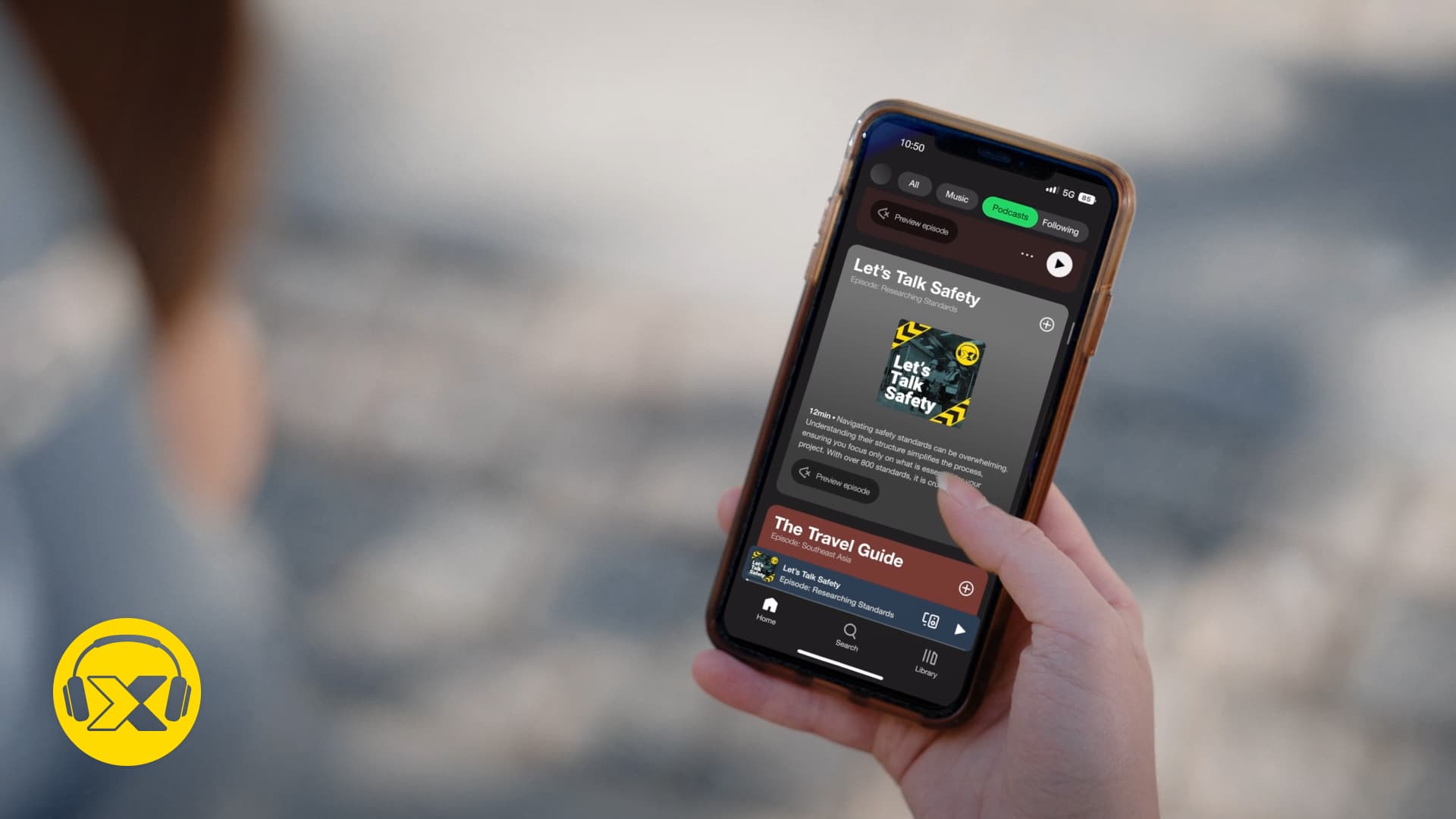 Una mano sosteniendo un smartphone que muestra un episodio de podcast titulado "Let's Talk Safety" en una aplicación de streaming.