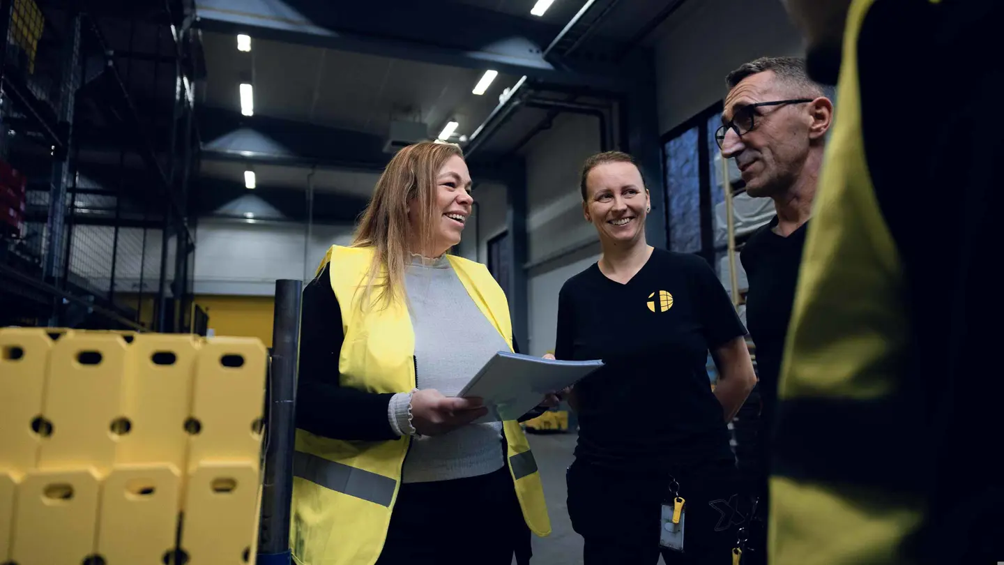 Employees at Axelent discussing industrial safety solutions in a warehouse setting. Emphasizing a strong safety culture with high-visibility gear and protective measures in place.